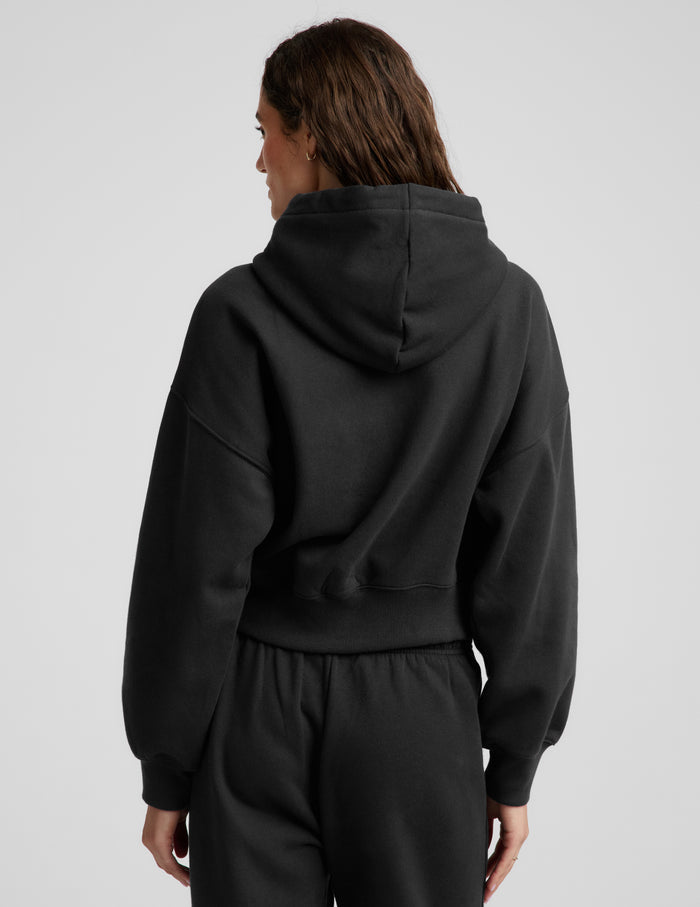 Woman wearing a black fleece zip-up sweatshirt and black sweatpants against a plain background.