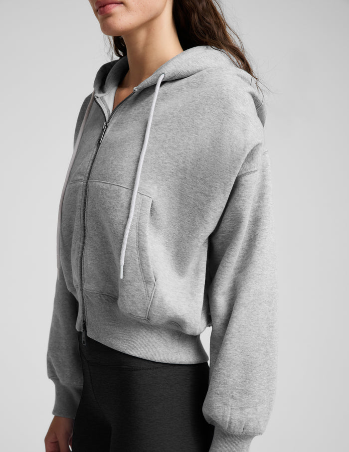 Woman wearing a green zip-up fleece sweatshirt and black leggings against a plain background.