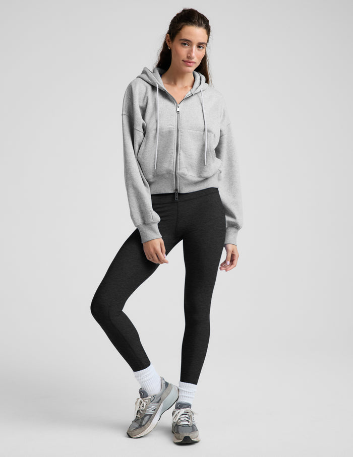 Woman wearing a green zip-up fleece sweatshirt and black leggings against a plain background.