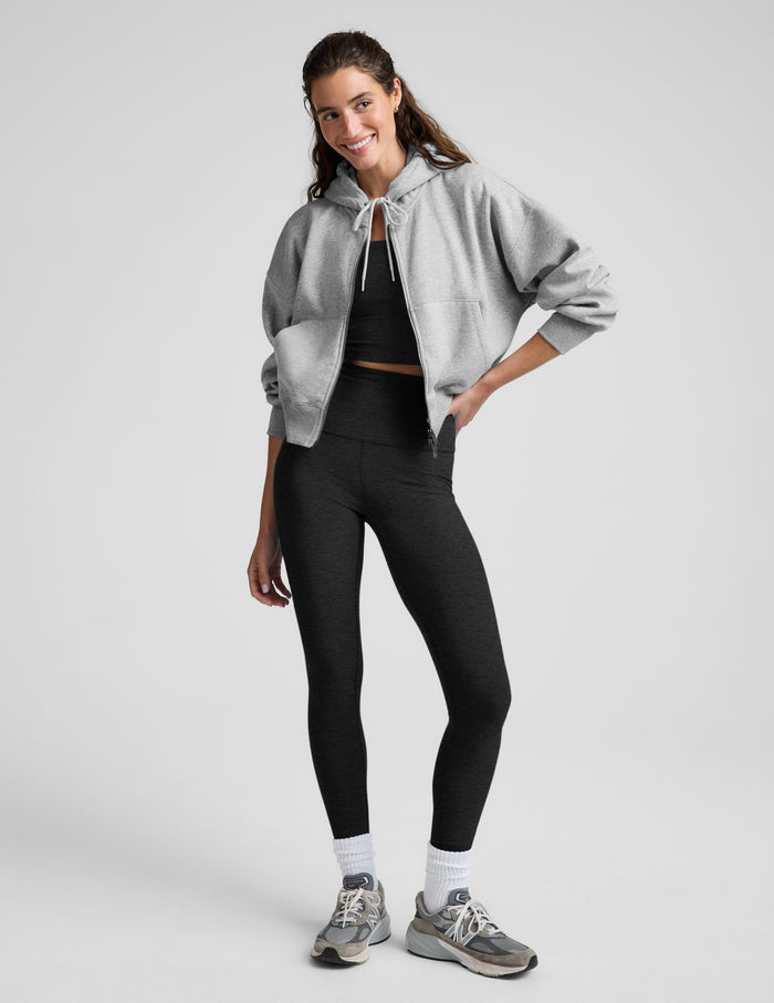 Woman wearing a green zip-up fleece sweatshirt and black leggings against a plain background.