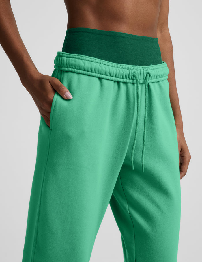Woman wearing a green bra and green joggers against a plain background.
