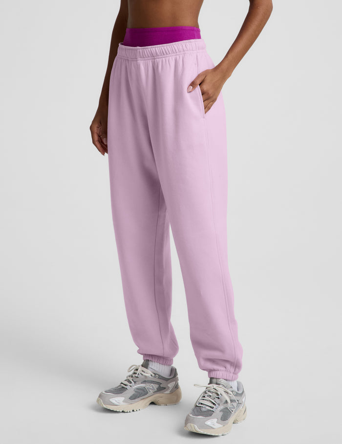 Woman wearing a purple bra and light purple fleece joggers against a plain background.