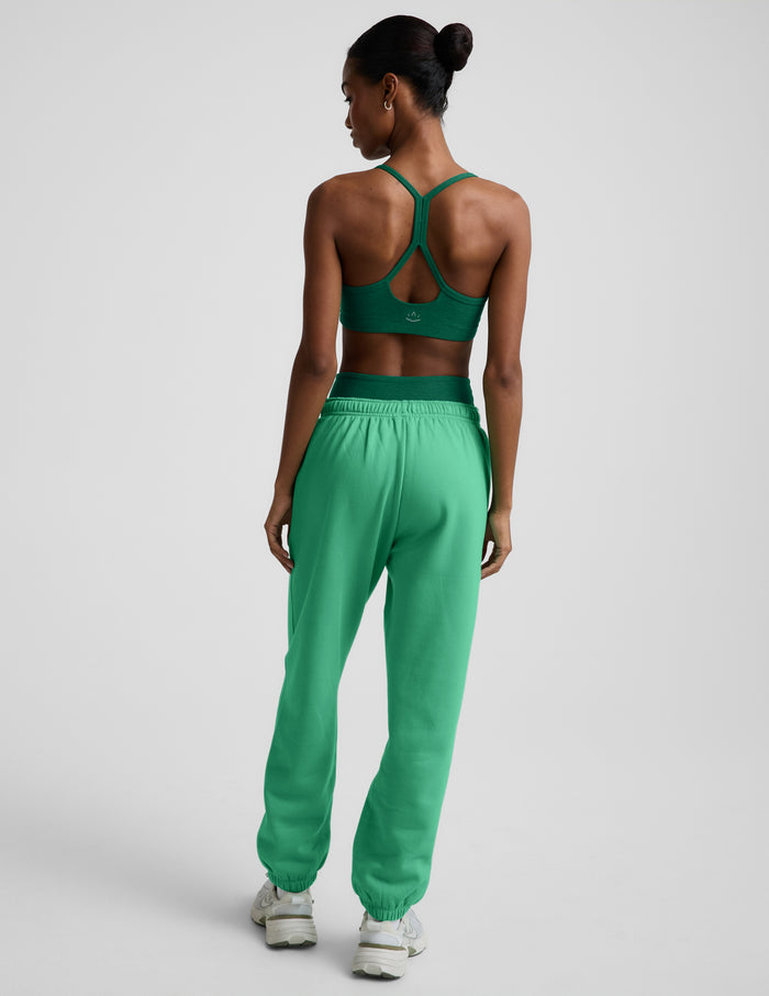 Woman wearing a green bra and green joggers against a plain background.