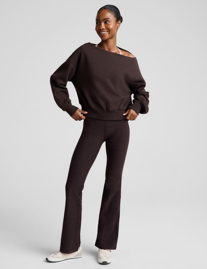 A woman modeling a dark brown off-the-shoulder sweatshirt and matching dark brown flared pants against a light gray studio background.