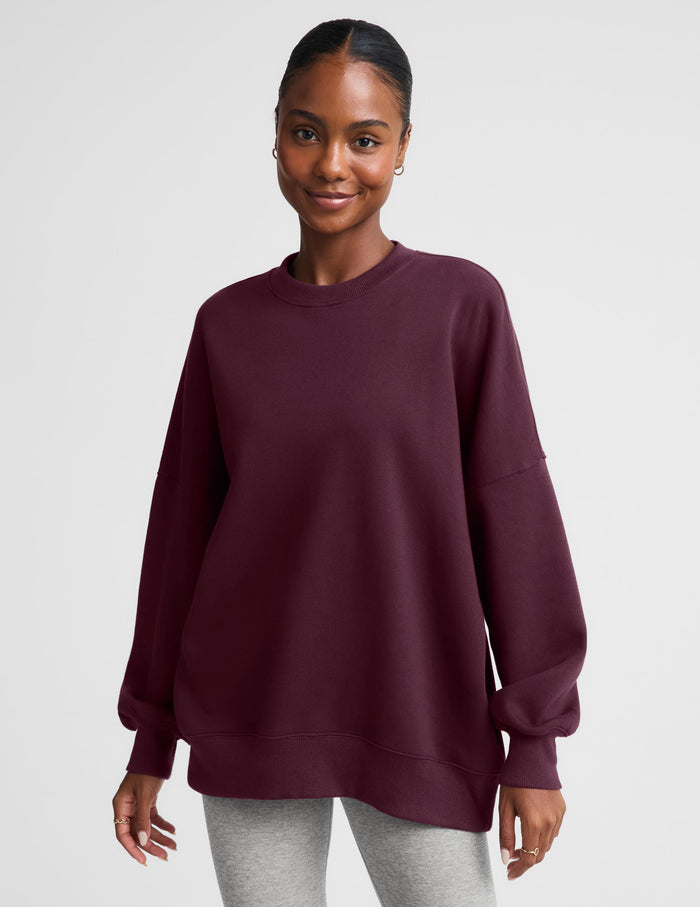 A woman modeling an oversized crewneck sweatshirt in deep burgundy, paired with light gray leggings, against a solid light gray background.