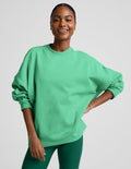 Woman wearing a green oversized crewneck sweatshirt and green leggings against a plain background.
