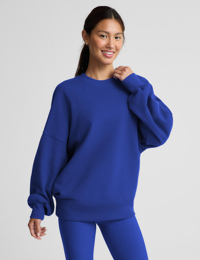 A woman modeling an oversized royal blue sweatshirt with matching blue leggings against a light gray studio background.
