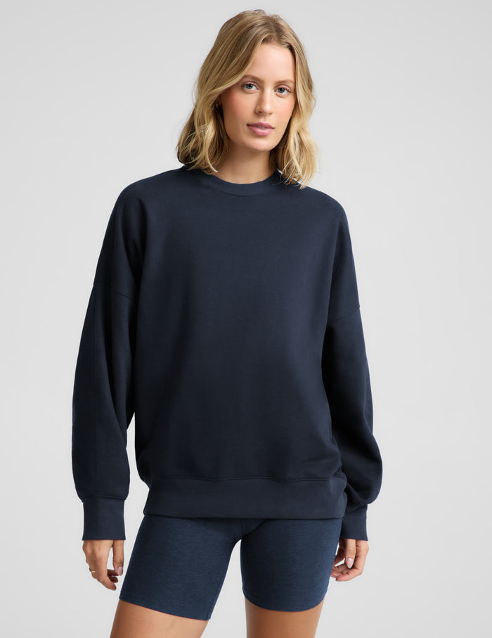 Woman wearing a navy blue oversized crewneck sweatshirt and biker shorts against a plain background.