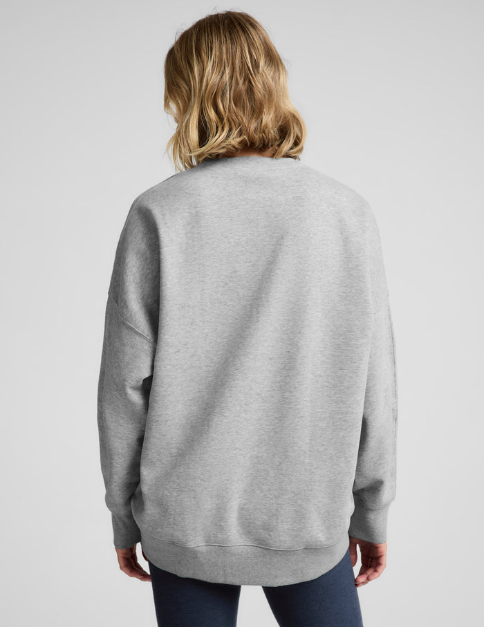 Woman wearing a gray oversized crewneck sweatshirt and navy blue leggings against a plain background.