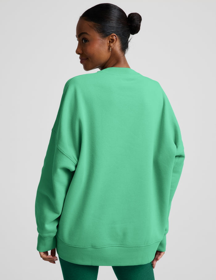 Woman wearing a green oversized crewneck sweatshirt and green leggings against a plain background.
