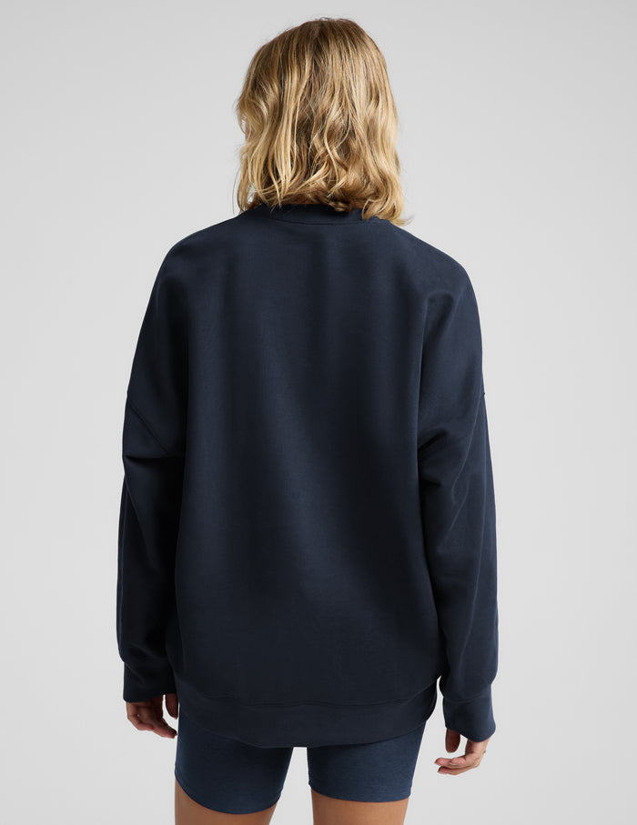 Woman wearing a navy blue oversized crewneck sweatshirt and biker shorts against a plain background.