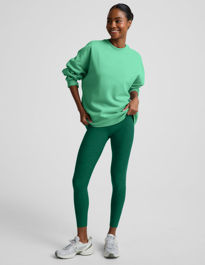 Woman wearing a green oversized crewneck sweatshirt and green leggings against a plain background.