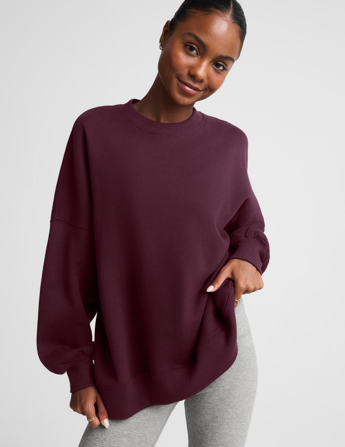 A woman modeling an oversized crewneck sweatshirt in deep burgundy, paired with light gray leggings, against a solid light gray background.