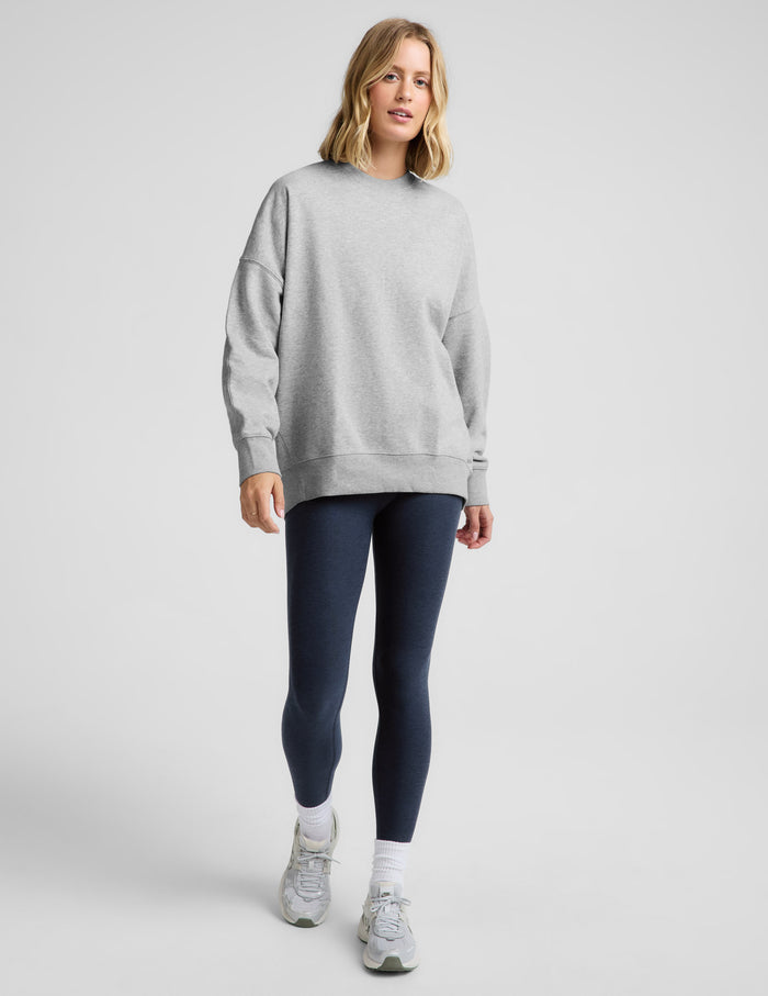 Woman wearing a gray oversized crewneck sweatshirt and navy blue leggings against a plain background.