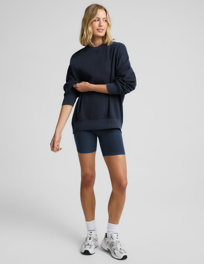 Woman wearing a navy blue oversized crewneck sweatshirt and biker shorts against a plain background.