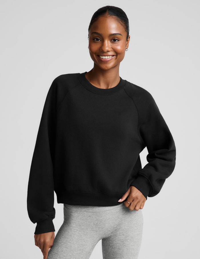 Woman wearing a black crewneck sweatshirt and gray pedal pushers against a plain background.