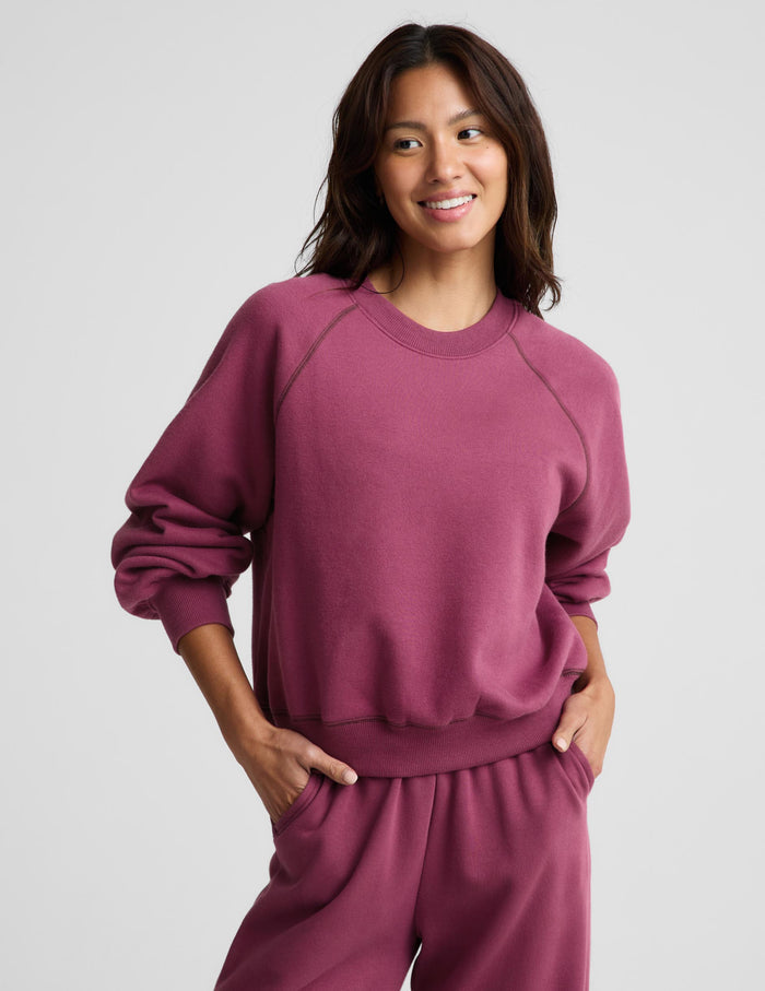 A woman modeling a matching dusty rose crewneck sweatshirt and jogger pants set against a light gray studio background.