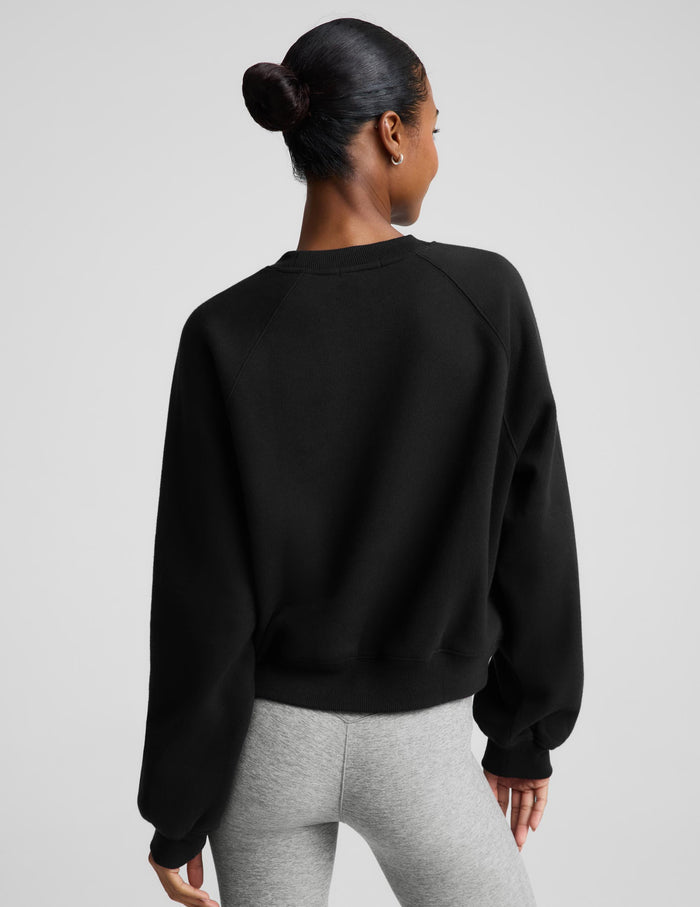 Woman wearing a black crewneck sweatshirt and gray pedal pushers against a plain background.