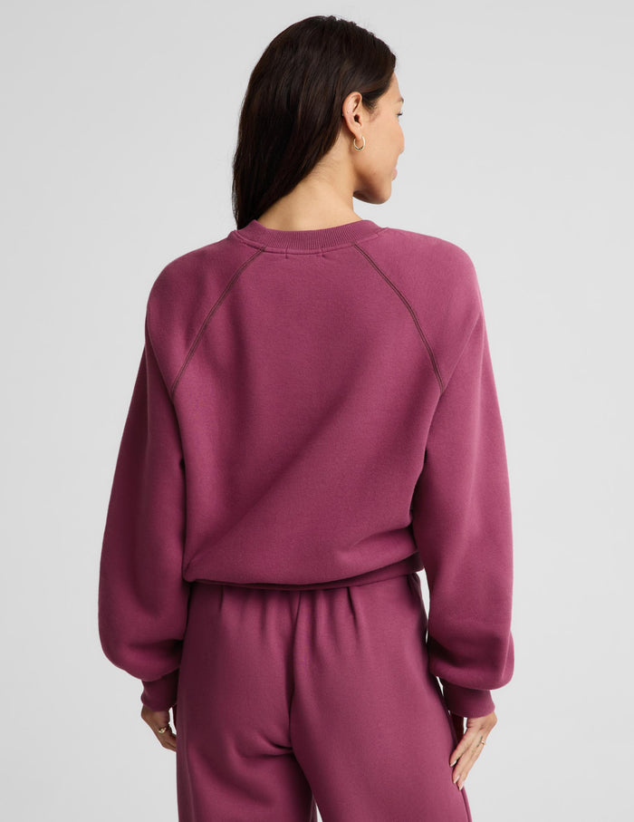A woman shown from the back wearing a matching dusty rose sweatshirt and sweatpants set against a plain light gray studio background.