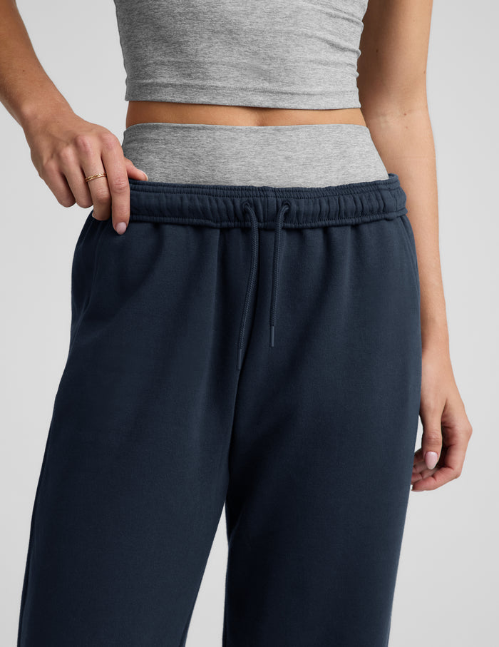 Woman wearing a gray tank top, gray biker shorts, and blue straight leg sweatpants against a plain background.