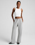 A woman modeling a white sleeveless crop top and light gray wide-leg sweatpants against a light gray studio background.