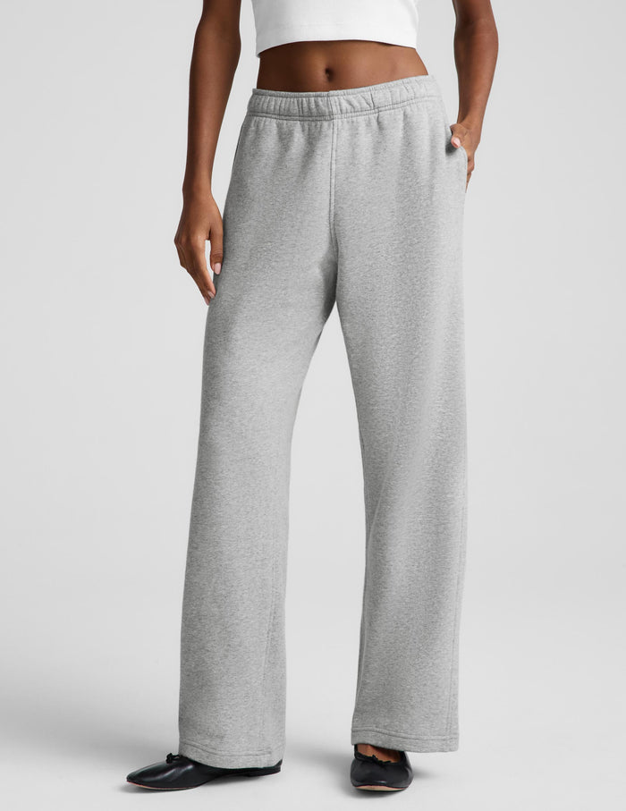 A woman modeling a white sleeveless crop top and light gray wide-leg sweatpants against a light gray studio background.