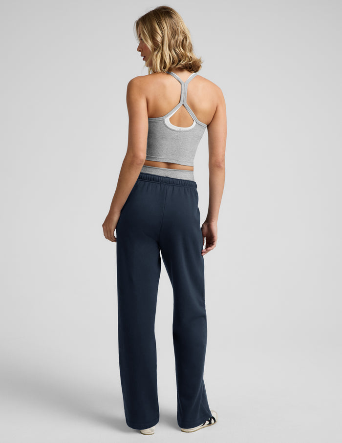 Woman wearing a gray tank top, gray biker shorts, and blue straight leg sweatpants against a plain background.