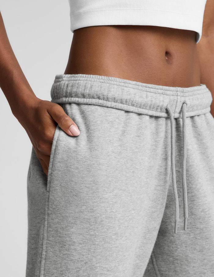 A woman modeling a white sleeveless crop top and light gray wide-leg sweatpants against a light gray studio background.