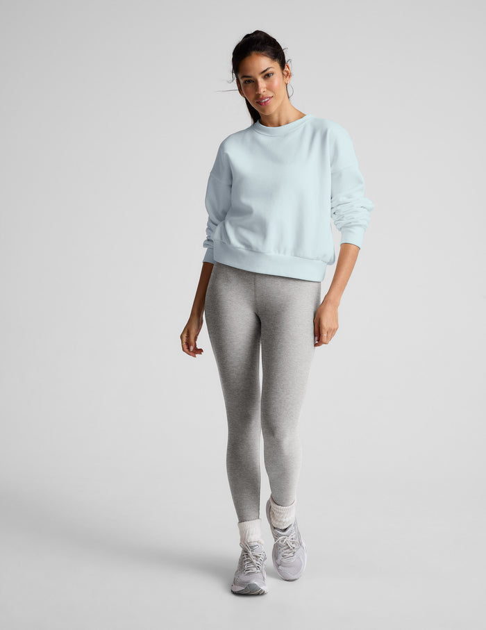 Woman wearing a light blue sweatshirt and gray leggings on a plain background.