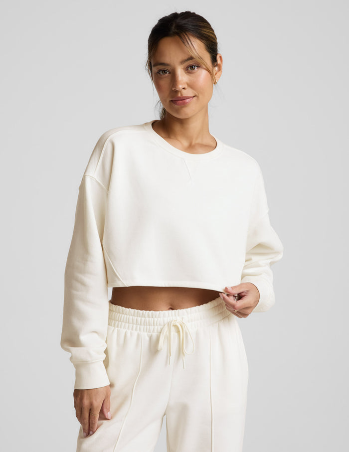 Woman wearing a white cropped sweatshirt and pants on a light gray background.