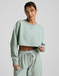 Woman wearing a light blue cropped sweatshirt and pants on a plain background.