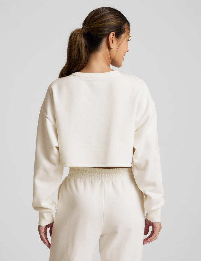 Woman wearing a white cropped sweatshirt and pants on a light gray background.