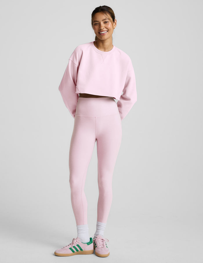 Woman wearing a pink sweatshirt and pants on a light gray background.