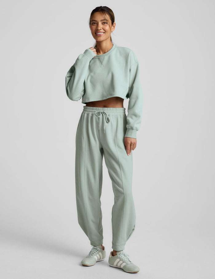 Woman wearing a light blue cropped sweatshirt and pants on a plain background.