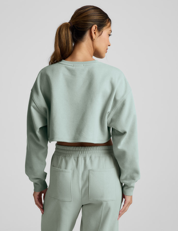 Woman wearing a light blue cropped sweatshirt and pants on a plain background.