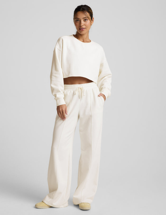 Woman wearing a white cropped sweatshirt and pants on a light gray background.
