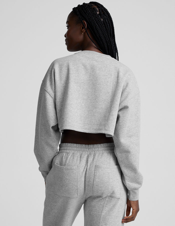 woman wearing a gray cropped sweatshirt and matching barrel fleece pants on a plain background.