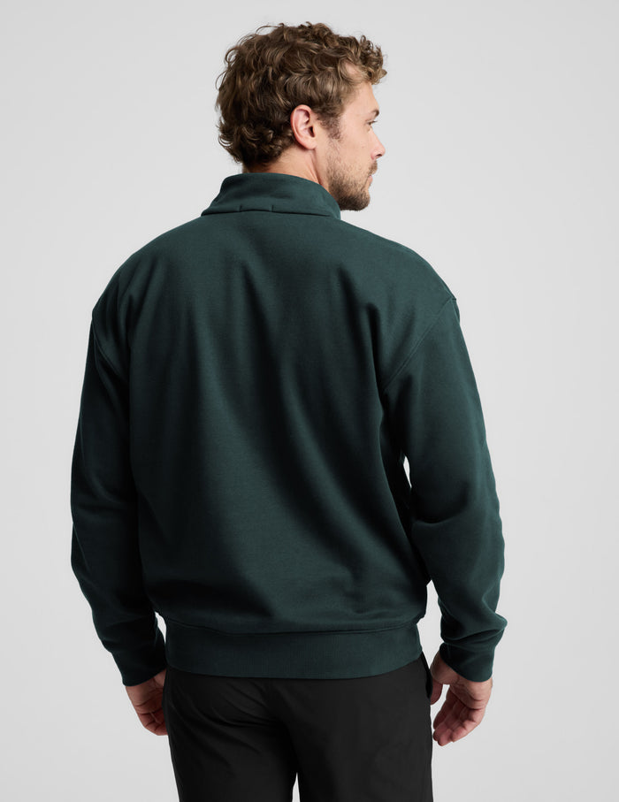 Man wearing a dark green quarter-zip sweatshirt and black shorts on a light gray background.