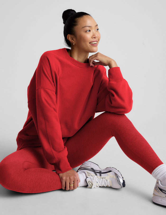 Woman wearing a red fleece sweatshirt and leggings sitting on the floor against a light gray background.