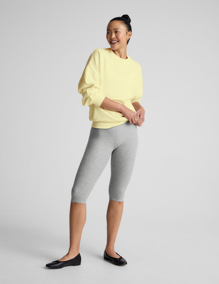 Woman wearing a light yellow sweatshirt and gray leggings on a plain background.