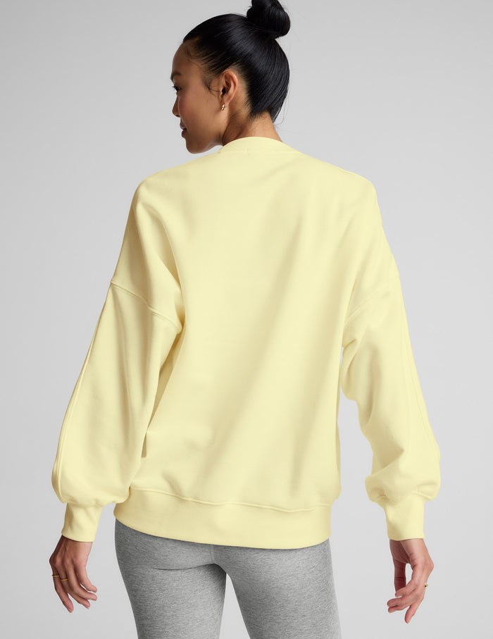 Woman wearing a light yellow sweatshirt and gray leggings on a plain background.
