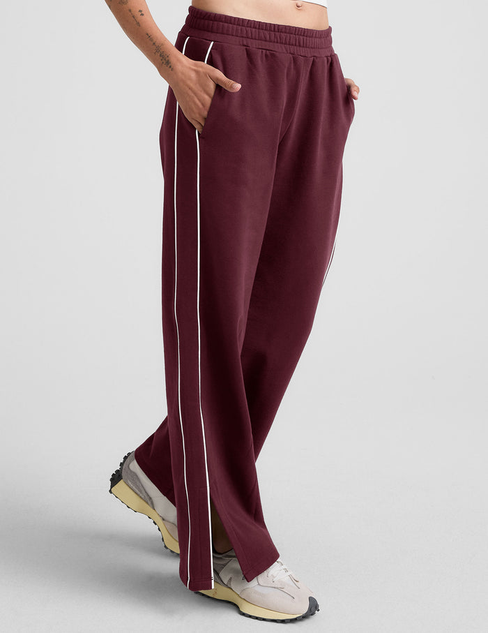 LuxeFleece Piper Wide Leg Pant in maroon with white side piping and hem slits, shown on a model at a 3/4 angle.