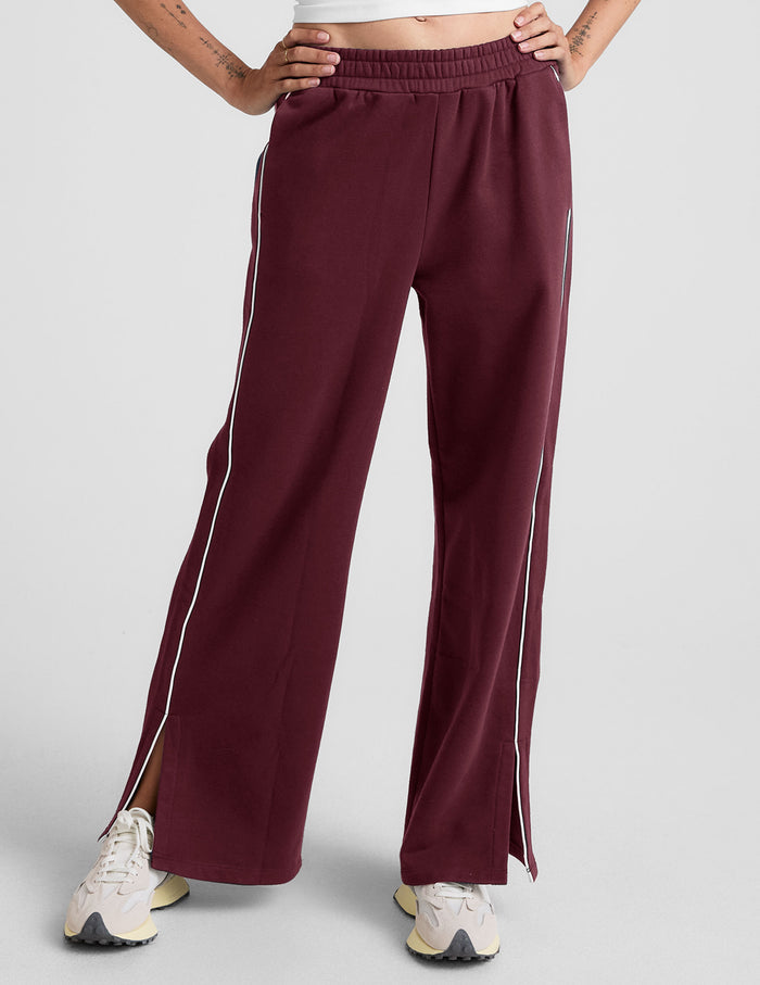 LuxeFleece Piper Wide Leg Pant in maroon featuring white side piping, ankle slits, and a relaxed, mid-rise fit on a model.