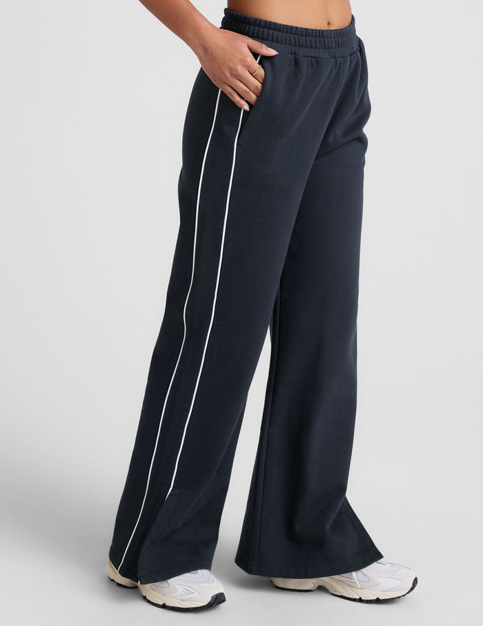 Model wearing LuxeFleece Piper Wide Leg Pant in navy with white side piping, elastic waist, and slant pockets.