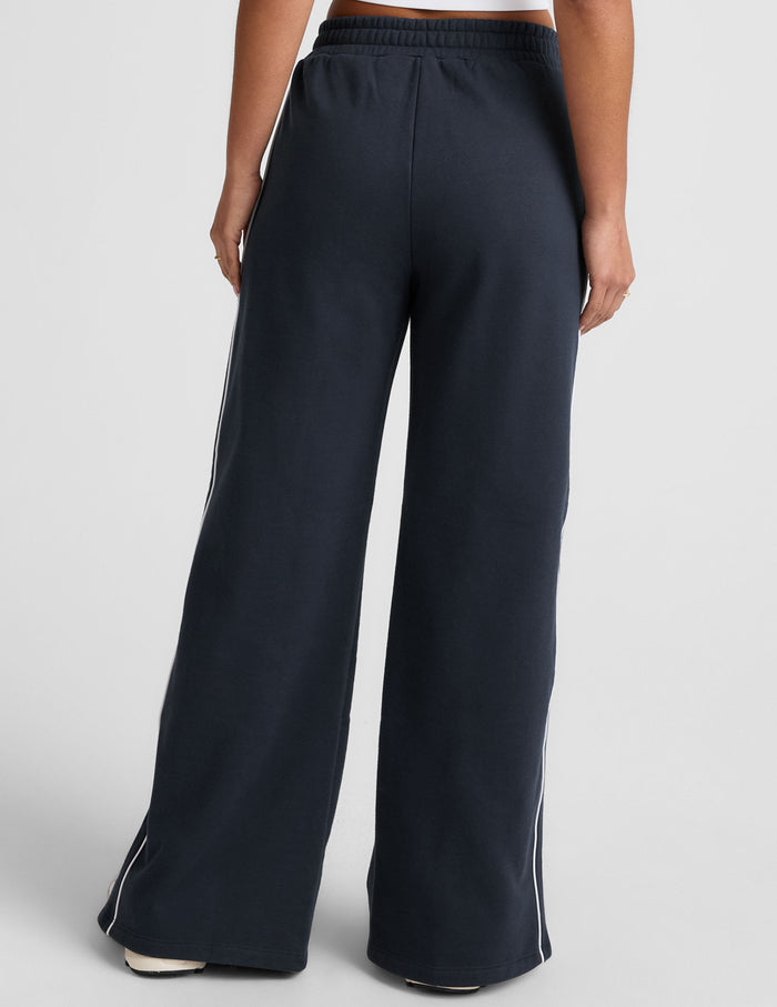 Rear view of navy LuxeFleece Piper Wide Leg Pant featuring white side piping and a relaxed, full-length silhouette.