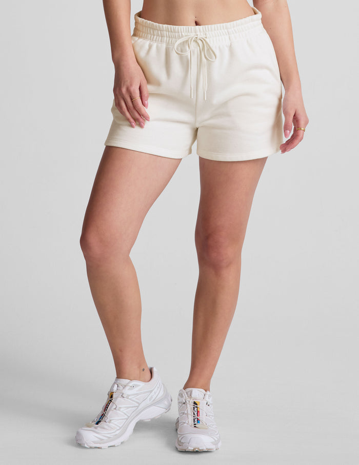 Cream LuxeFleece Sweat Short on model, featuring an elastic drawstring waistband, relaxed fit, and side pockets.