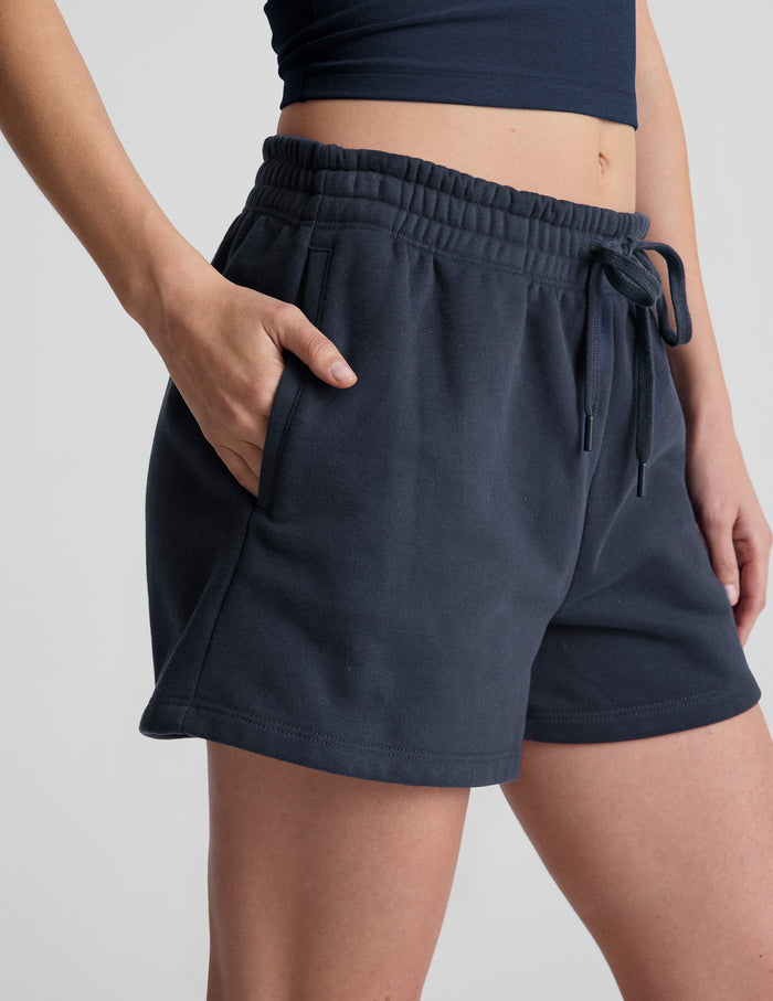 Navy LuxeFleece Sweat Short with an elastic drawstring waistband and side pockets on a model.