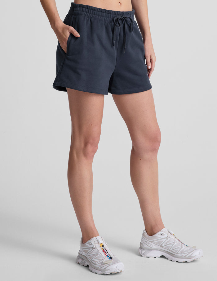 Navy LuxeFleece Sweat Short with drawstring elastic waist and side pockets, shown on a model in a relaxed mid-rise fit.