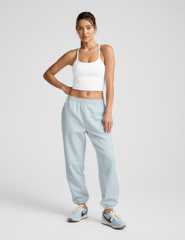 Woman wears light blue LuxeFleece Sweatpant with relaxed fit, elastic waistband, and ankle cuffs against a grey backdrop.