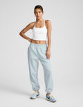 Woman wears light blue LuxeFleece Sweatpant with relaxed fit, elastic waistband, and ankle cuffs against a grey backdrop.
